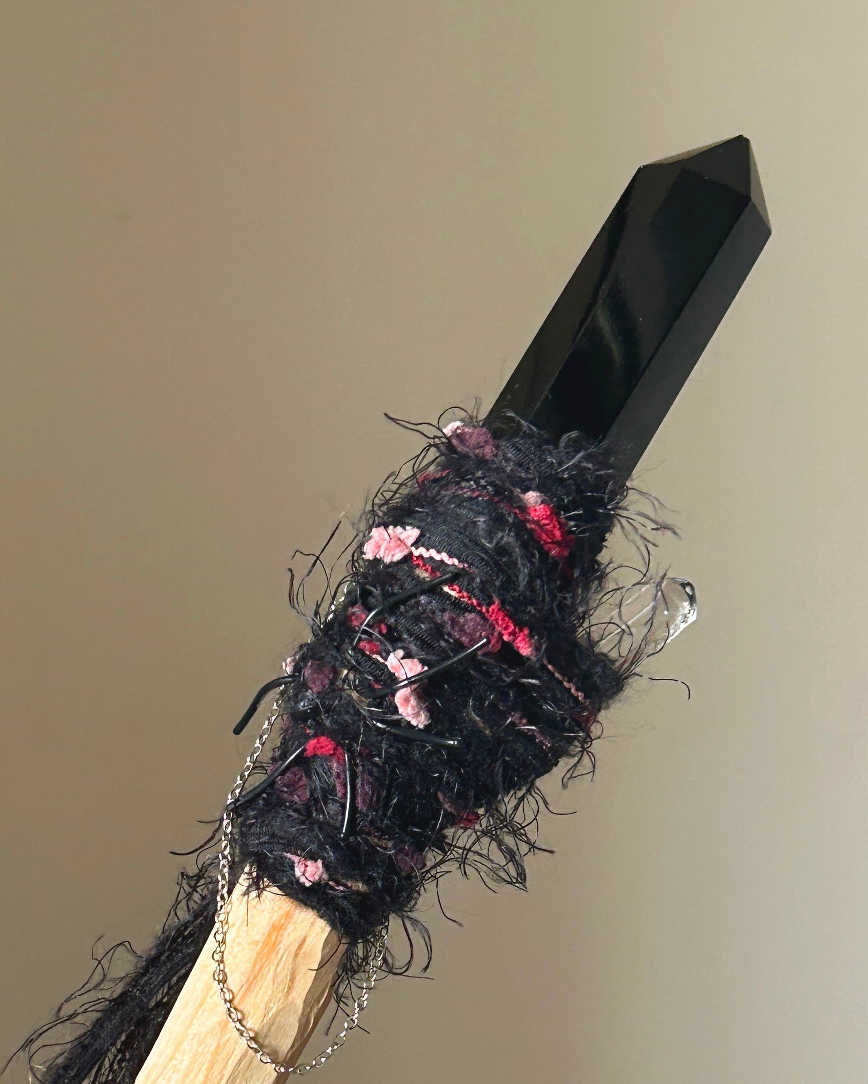 Front view of obsidian wand with spiderweb charm and black-red binding
