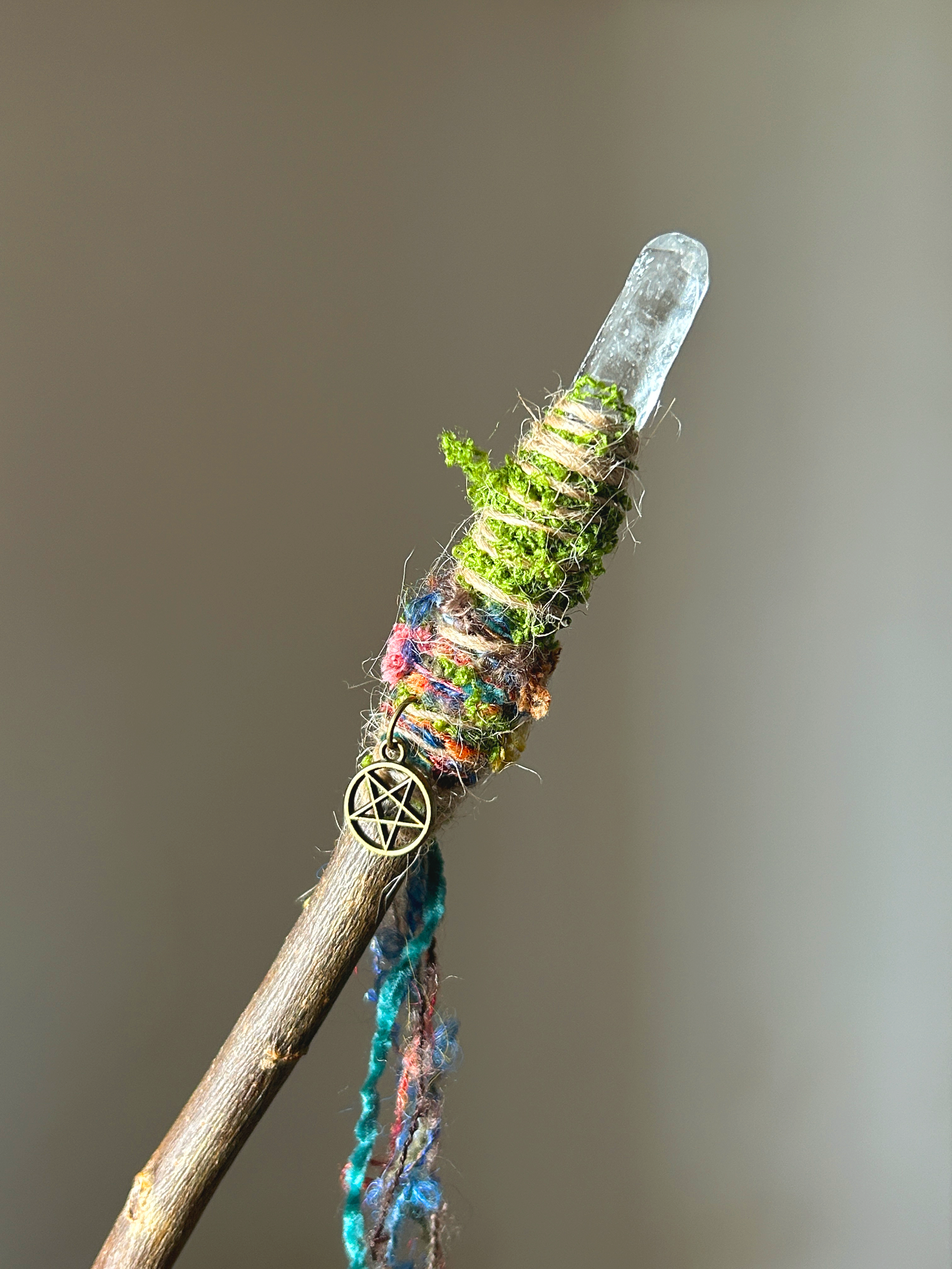 Close-up of quartz point and multicolored fibers with moss and pentacle charm