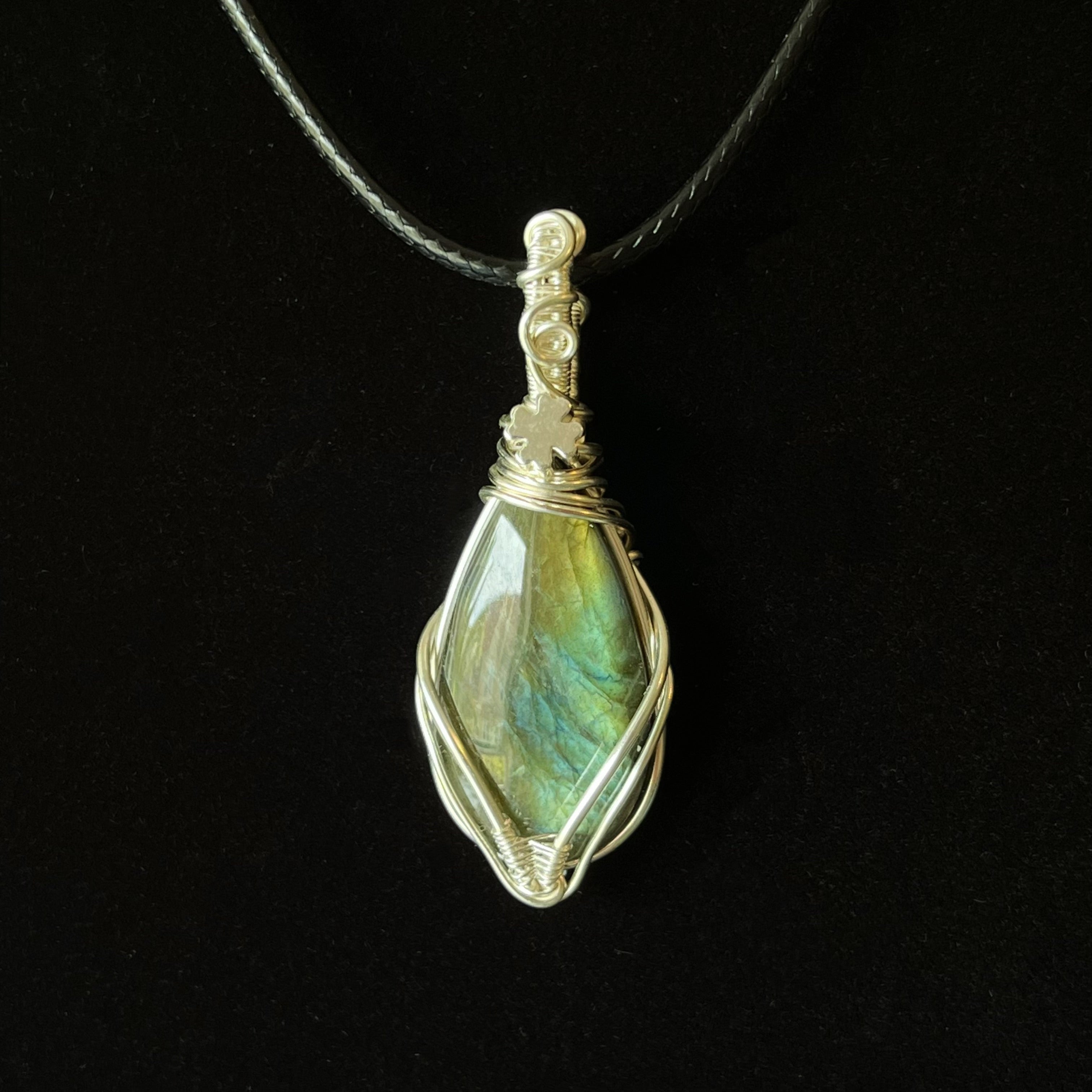 Shield-shaped green-blue labradorite pendant wrapped in twisting silver wire with crest detail