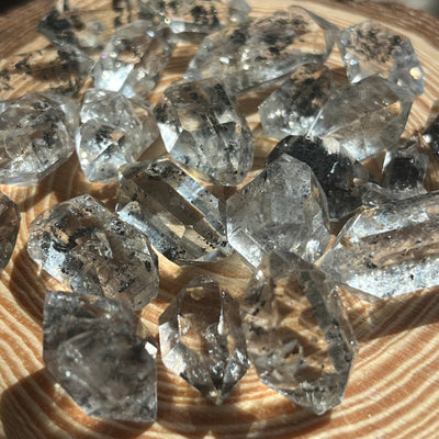A–AA grade transparent Elestial Quartz crystals with hydrocarbon inclusions displayed on a wooden slab.